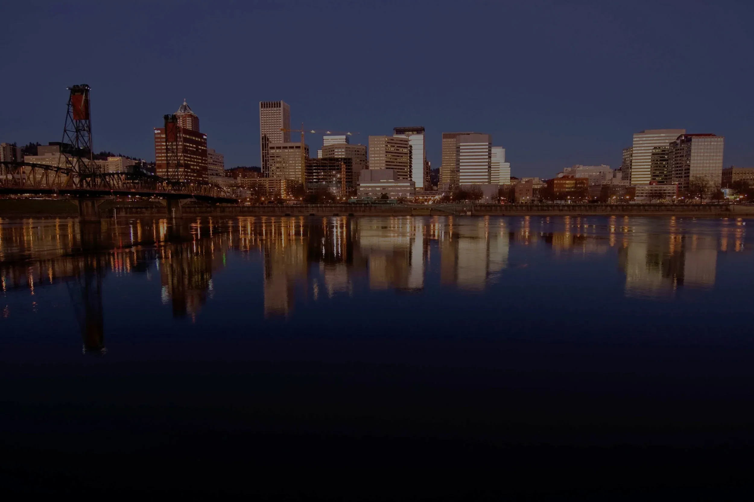 Downtown Portland at night, its lights reflected in the river below.